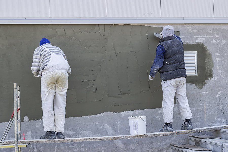 Two workers applying gray plaster to an exterior wall at a construction site