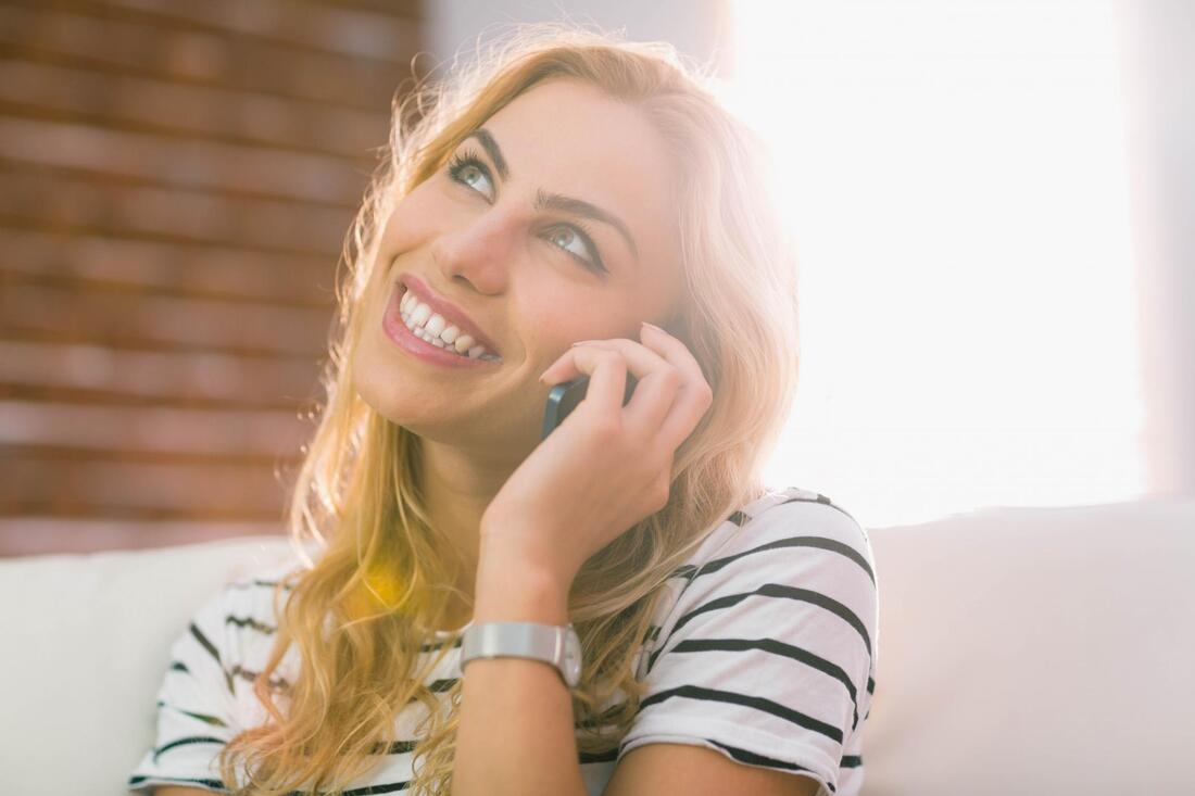Smiling woman on a phone call, wearing a striped shirt in bright sunlight