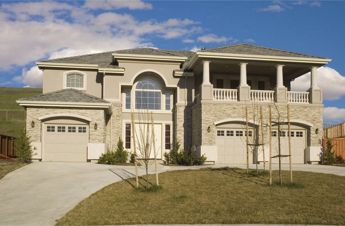 Large beige two-story suburban house with a front lawn and two garages under a blue sky
