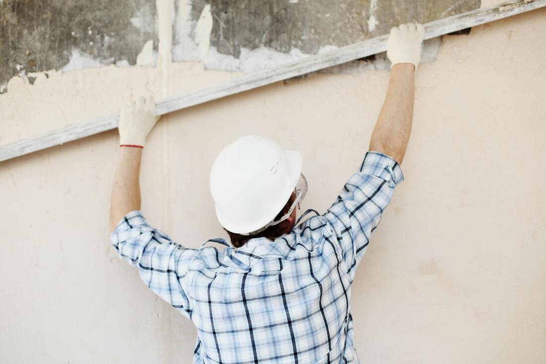 Worker in white hard hat inspecting a wall with arms raised
