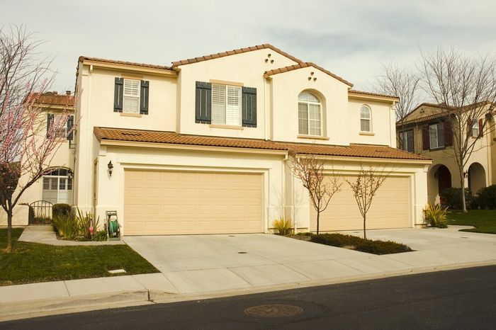 Suburban two-story beige house with a three-car garage and a front lawn at dusk