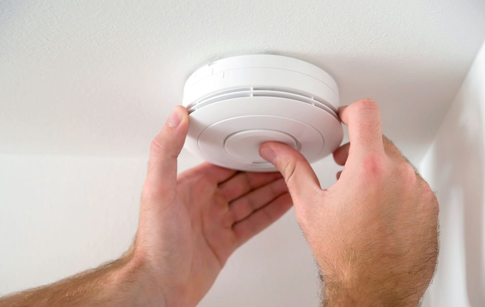 Person Installs White Smoke Detector on a White Ceiling — NTR Electrical In Maryborough, QLD