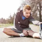 Man kneeling on pavement, examining a small white dog outdoors.