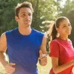Two runners jogging outdoors in bright shirts, smiling in a sunny park