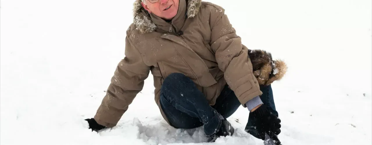 Two people crouching in snow, one wearing a brown coat and smiling.