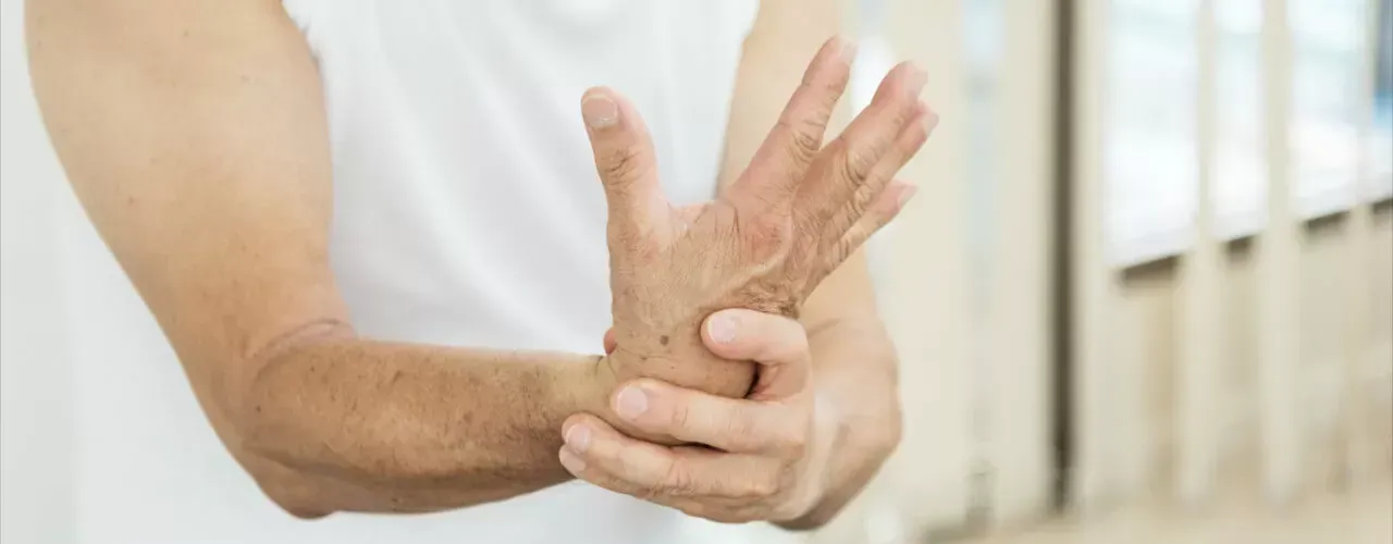 Person holding a bent, swollen hand at the wrist, suggesting pain or injury