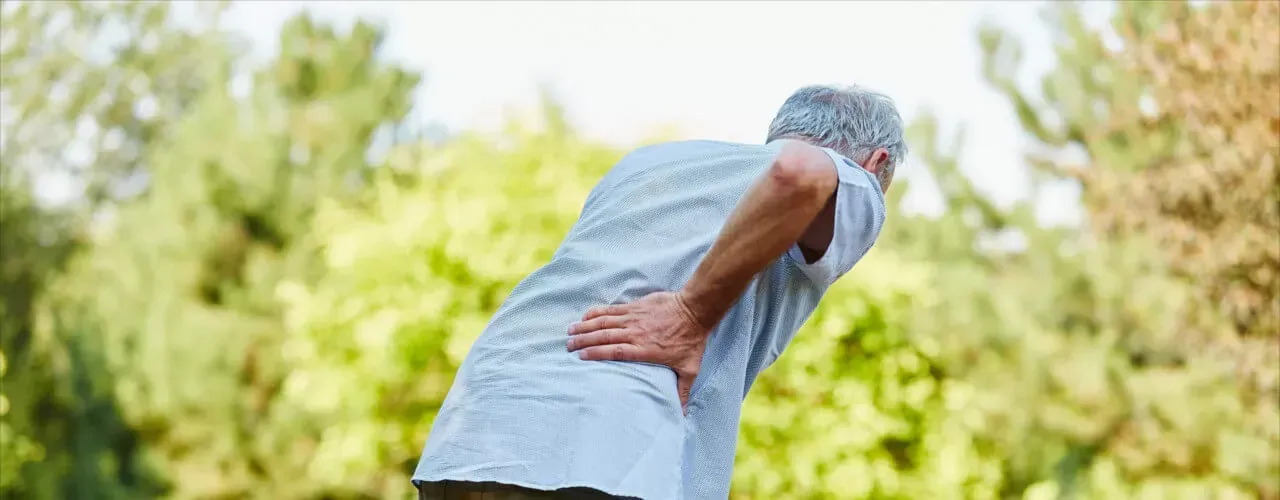 Person bent over holding lower back in a sunny outdoor setting