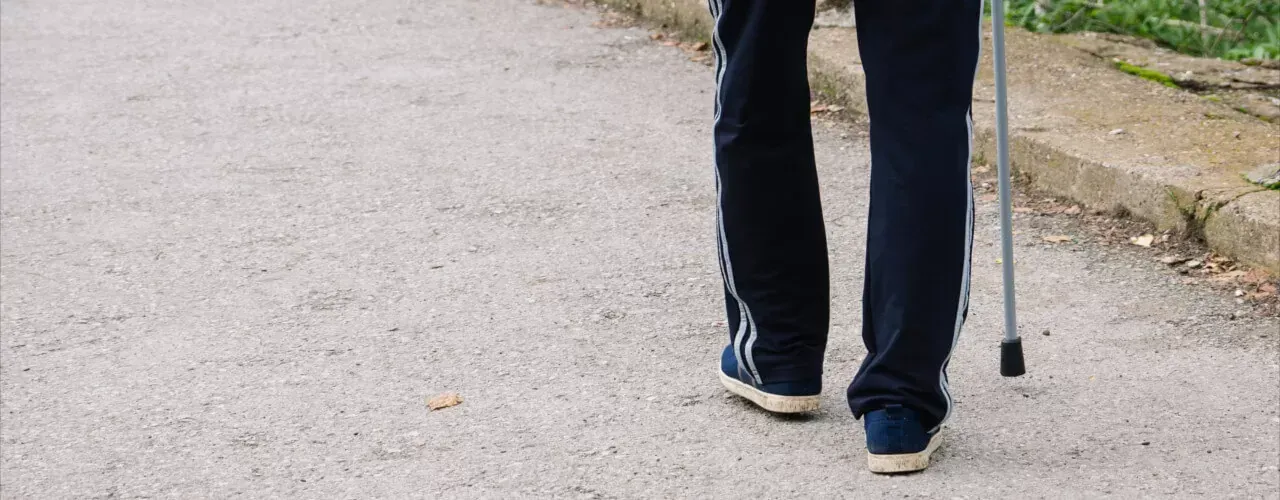 Person walking on a paved path with a cane, seen from behind.
