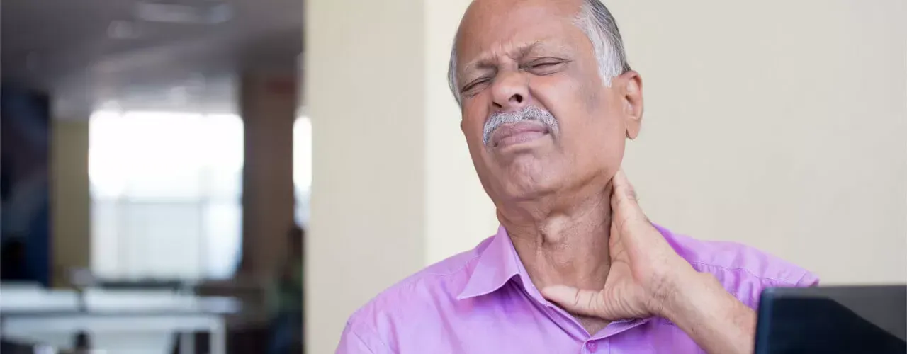 Man holding his neck in pain, wearing a purple shirt indoors