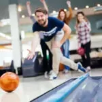 Man aiming a bowling ball down a lane while others watch in a bowling alley
