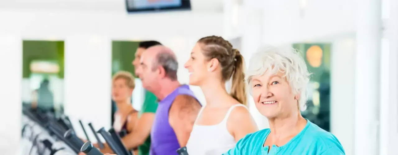People exercising on treadmills in a bright gym, with an older woman in the foreground