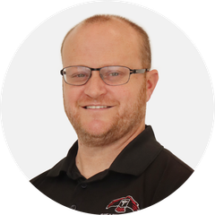 Portrait of a smiling person wearing glasses and a black polo shirt with a logo