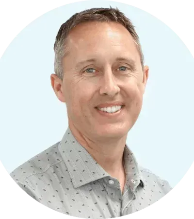 Smiling man in a light gray patterned shirt against a pale blue background