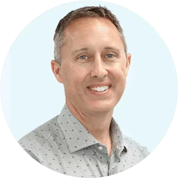 Smiling man in a light gray patterned shirt on a pale blue circular background