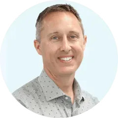 Portrait of a smiling man in a light gray patterned shirt on a pale blue background