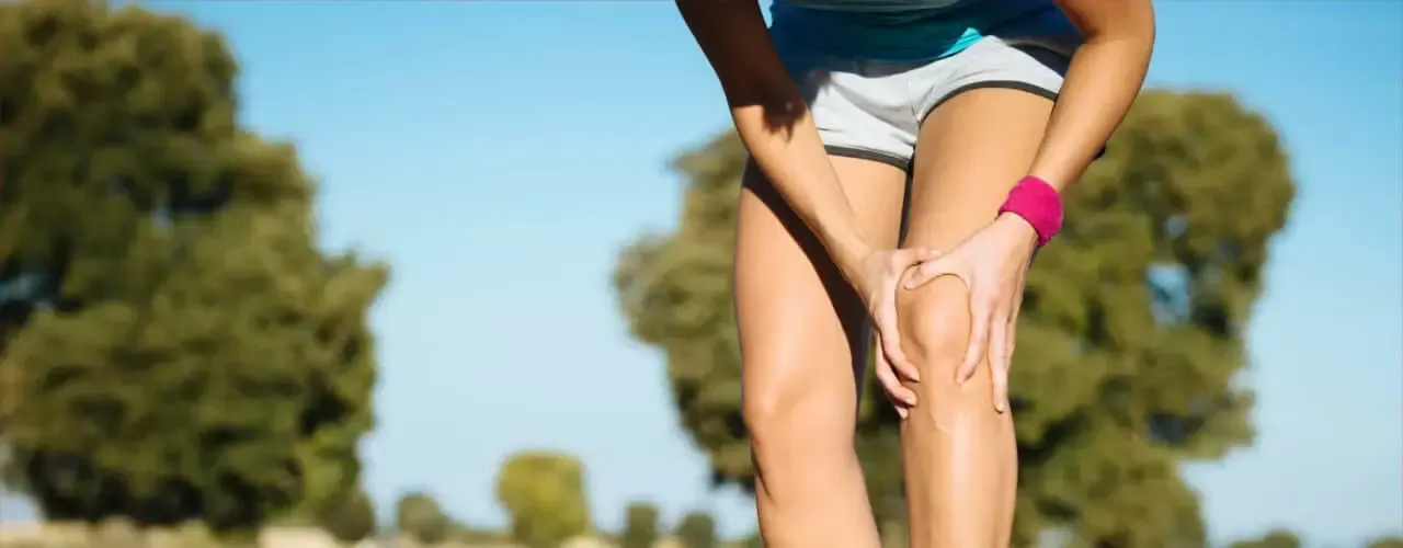Runner bending over outdoors and holding her knee on a sunny path