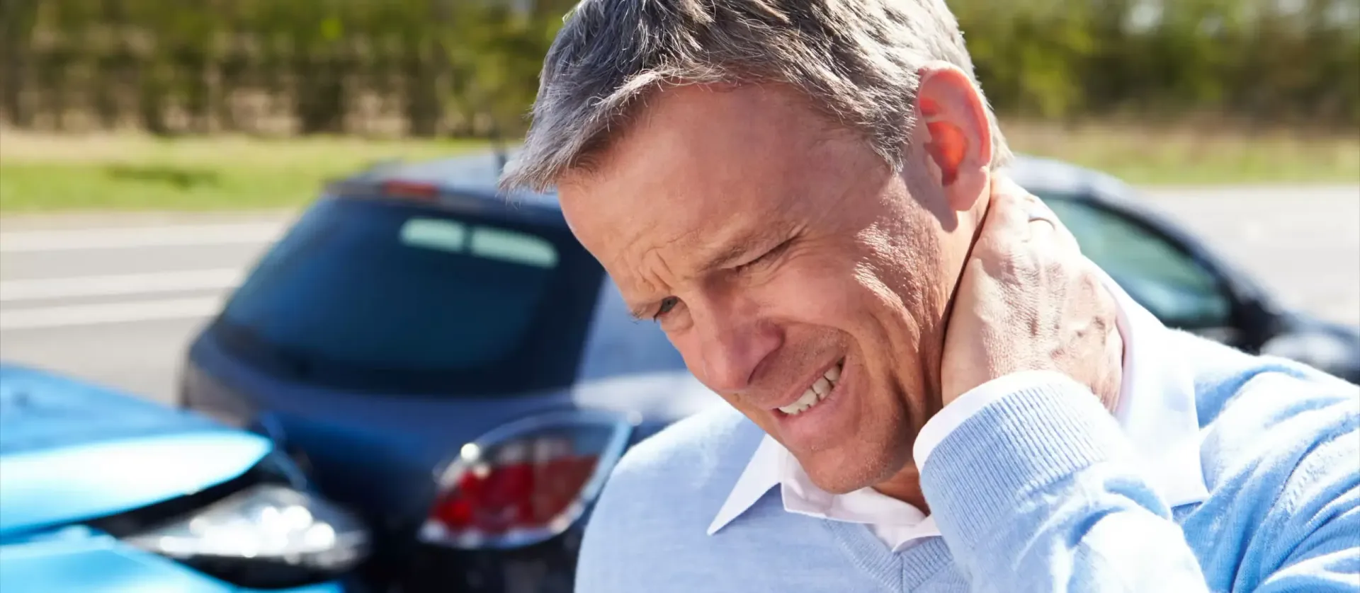 Man holding his neck in pain near parked cars outdoors