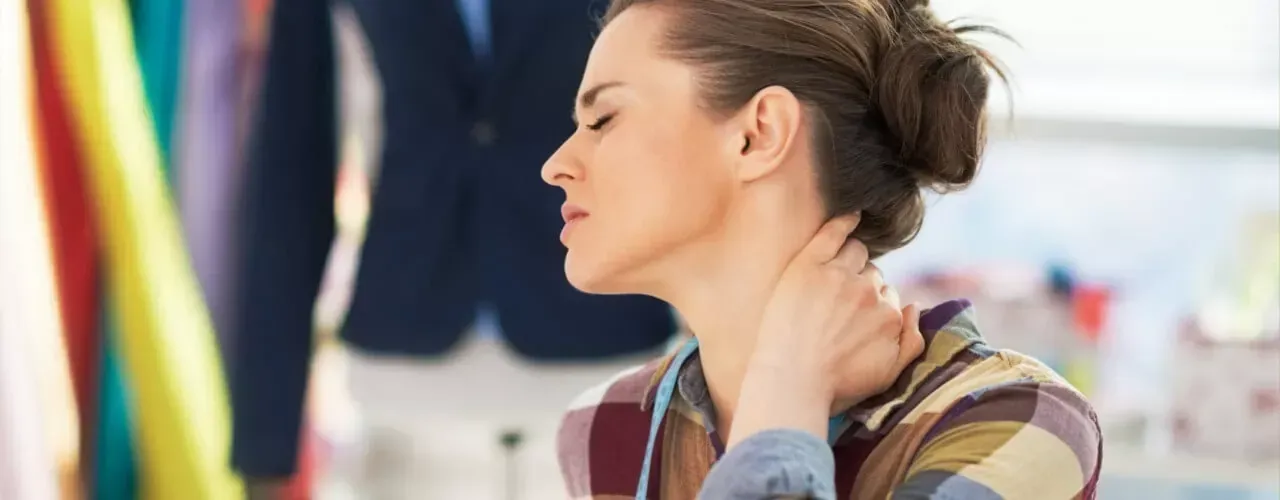 Woman rubbing her neck in a clothing store, with colorful garments in the background
