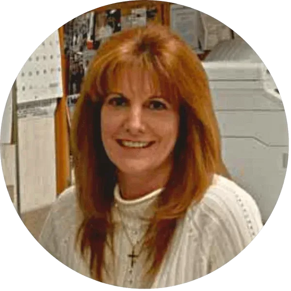 Smiling woman with red hair in a white sweater, standing indoors near office papers