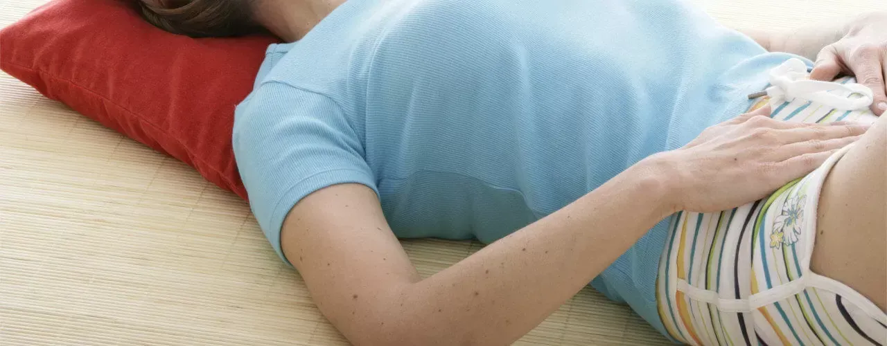 Person lying on a bed with a red pillow, wearing a light blue shirt and striped shorts