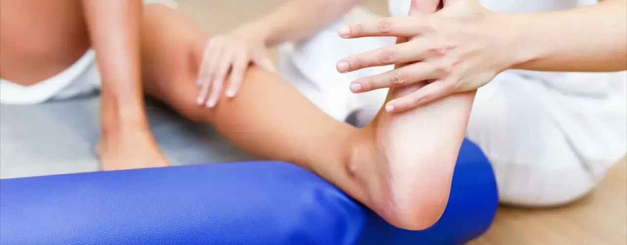 Hands supporting a person’s leg on a blue foam roller during physical therapy stretch