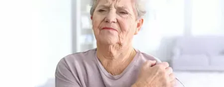 Older adult holding shoulder with a pained expression in a bright room