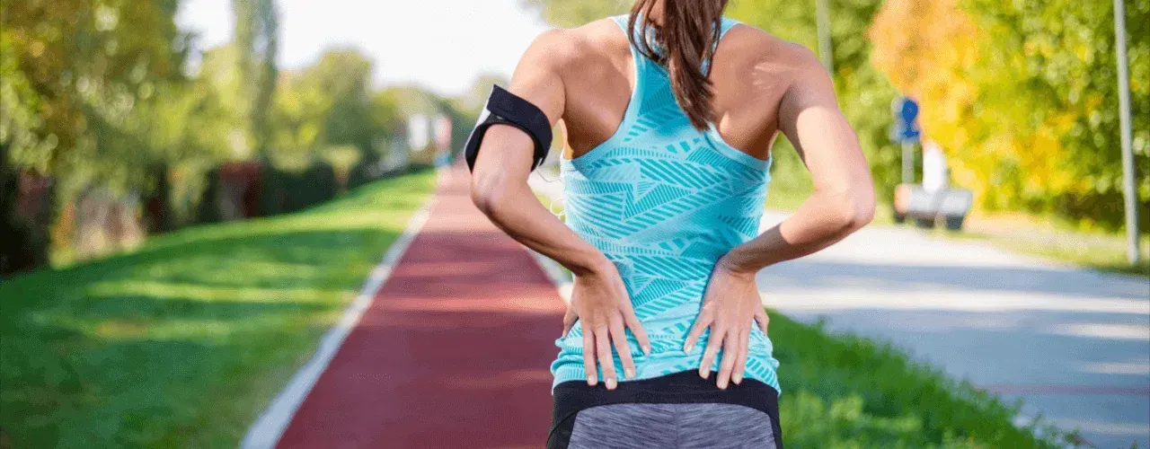 Person jogging on a red track with hands on their lower back, wearing a blue top.