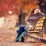 Woman sitting on a yellow park bench in autumn leaves, leaning back and looking relaxed