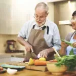 Person cooking vegetables in a kitchen, slicing food on a cutting board with fresh produce nearby