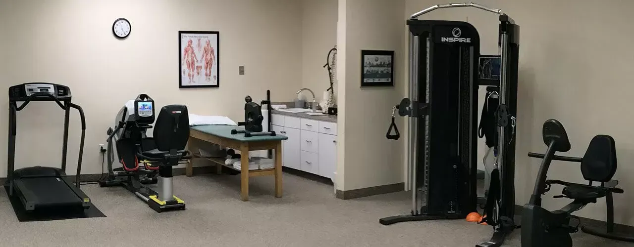 Small gym room with exercise machines, a table, wall art, and an office chair.