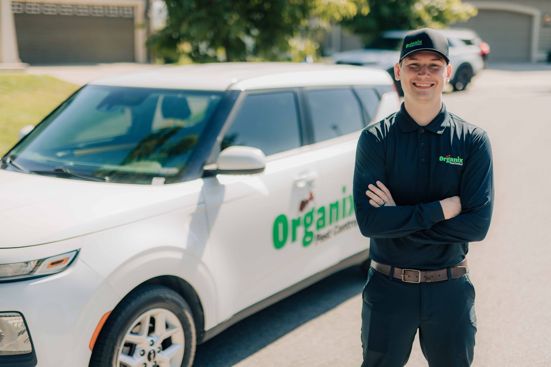 Man in black uniform, arms crossed, smiles by white car with