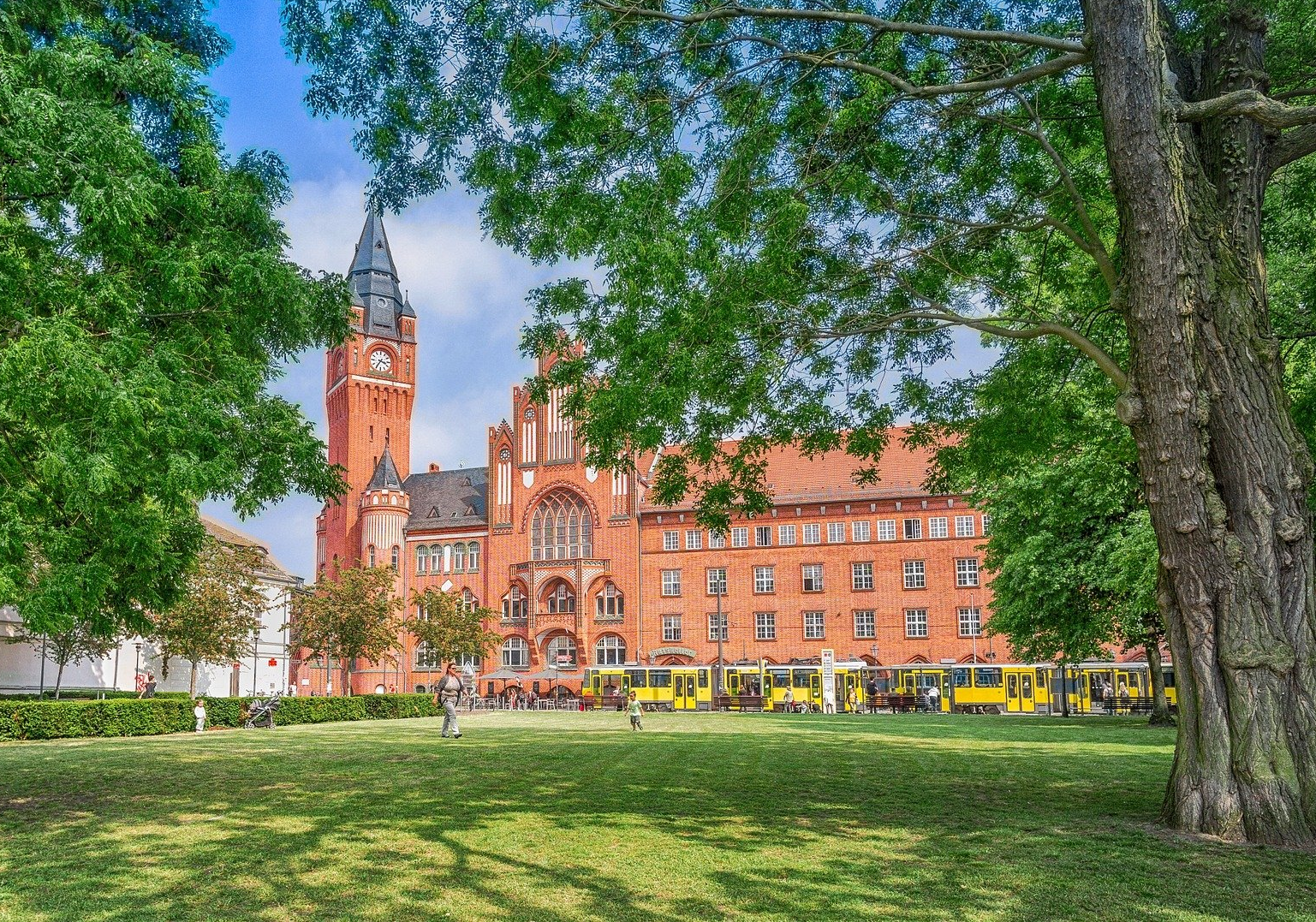 Ein großes rotes Backsteingebäude mit einem Uhrenturm ist von Bäumen in einem Park umgeben.
