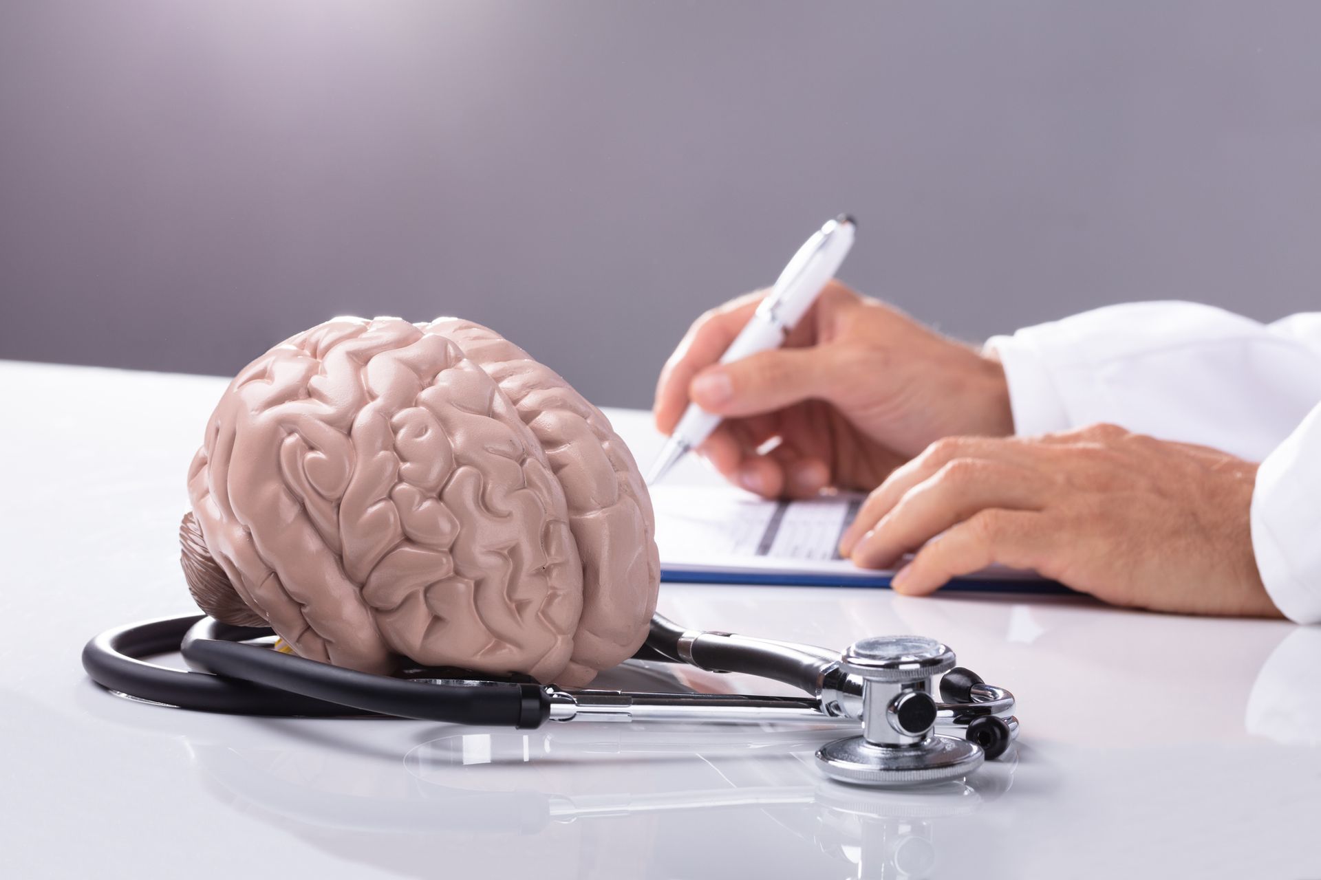 A doctor is writing on a clipboard next to a model of a brain and a stethoscope.