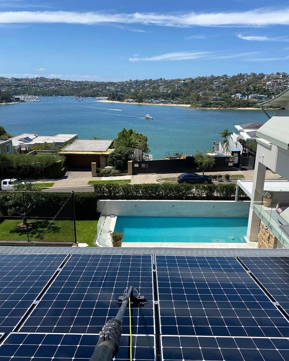 A Row Of Solar Panels On A Roof Overlooking A Pool And A Body Of Water — Freshwater Exterior Cleaning in Lennox Head, NSW