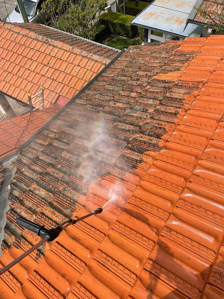 A Person Is Cleaning A Tiled Roof With A High Pressure Washer — Freshwater Exterior Cleaning in Lennox Head, NSW