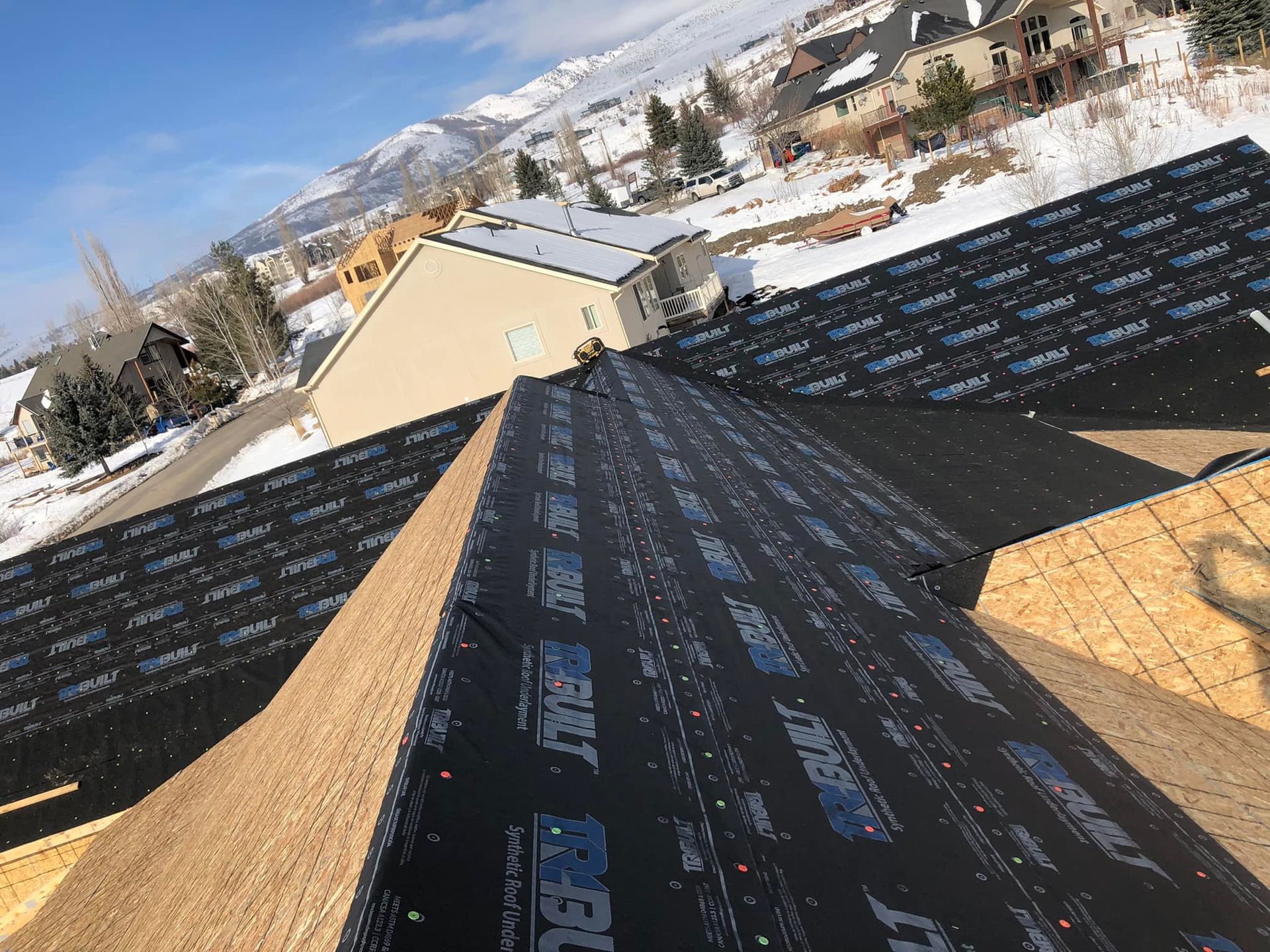 The roof of a house is being covered with a black roofing material.