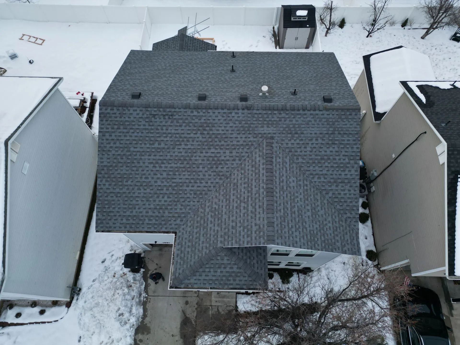 Overhead view of a house with a gray shingled roof, surrounded by snow.
