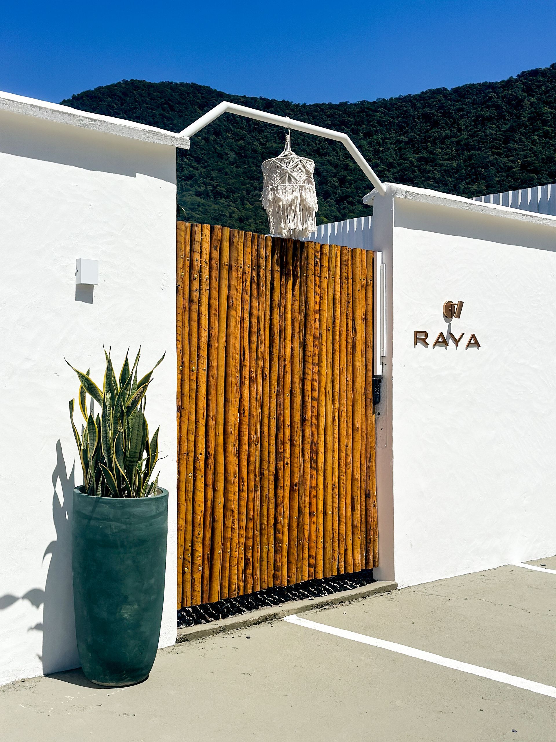 Portão branco com ripas de madeira, lanterna pendurada, planta em vaso e placa 