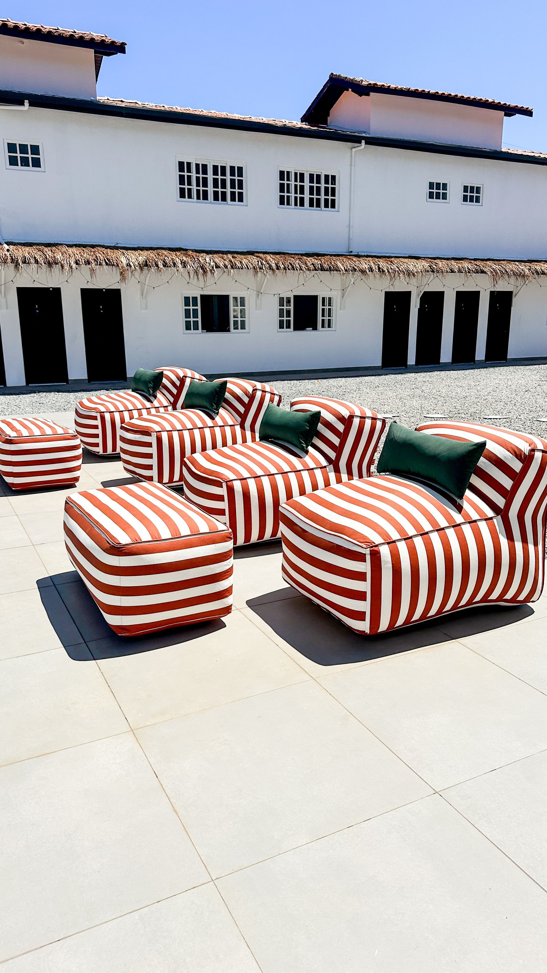 Cadeiras de descanso listradas em vermelho e branco em um pátio ensolarado em frente a um prédio branco.