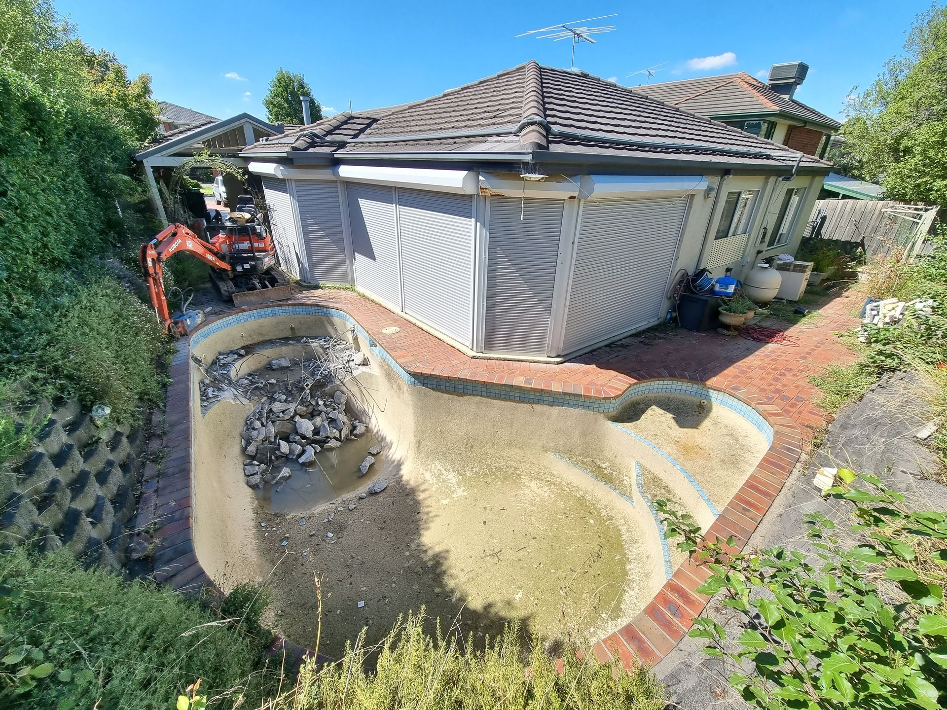 An Empty, Debris-filled Swimming Pool Under Construction Next to a House — All Over Pool Removals in Upwey, VIC