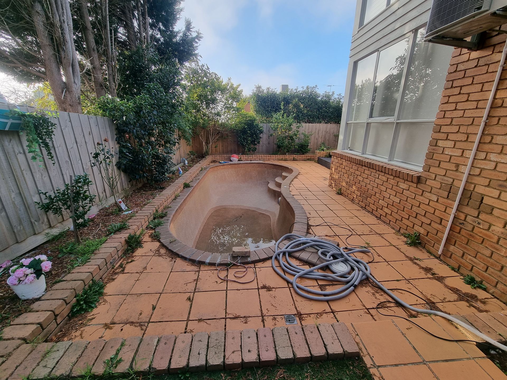 An Empty Backyard Pool With Tan Paving Stones, Adjacent to a Brick House — All Over Pool Removals in Beaumaris, VIC