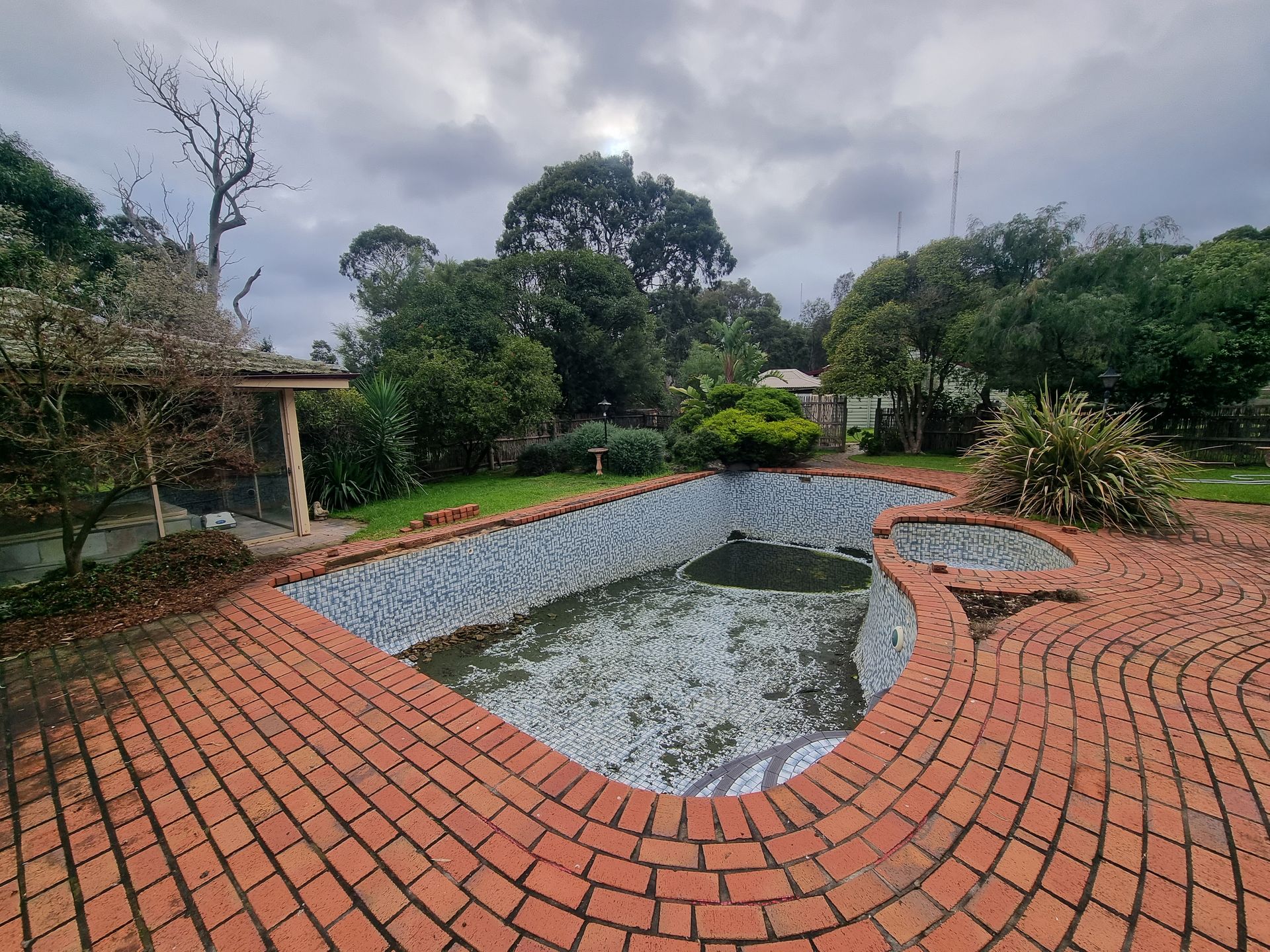 An Empty, Tiled Swimming Pool Surrounded by a Brick Patio — All Over Pool Removals in Glen Waverley, VIC