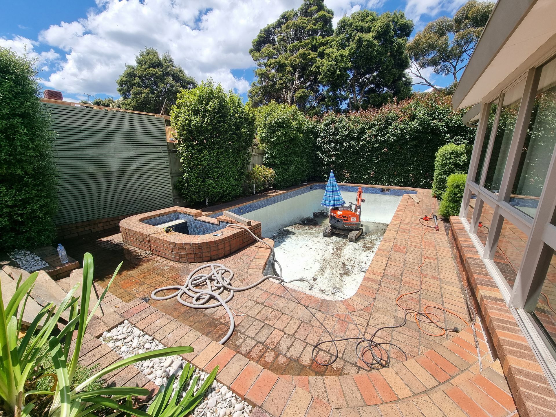 A Small Orange Excavator Sits Inside an Empty Backyard Swimming Pool Undergoing — All Over Pool Removals in Beaumaris, VIC