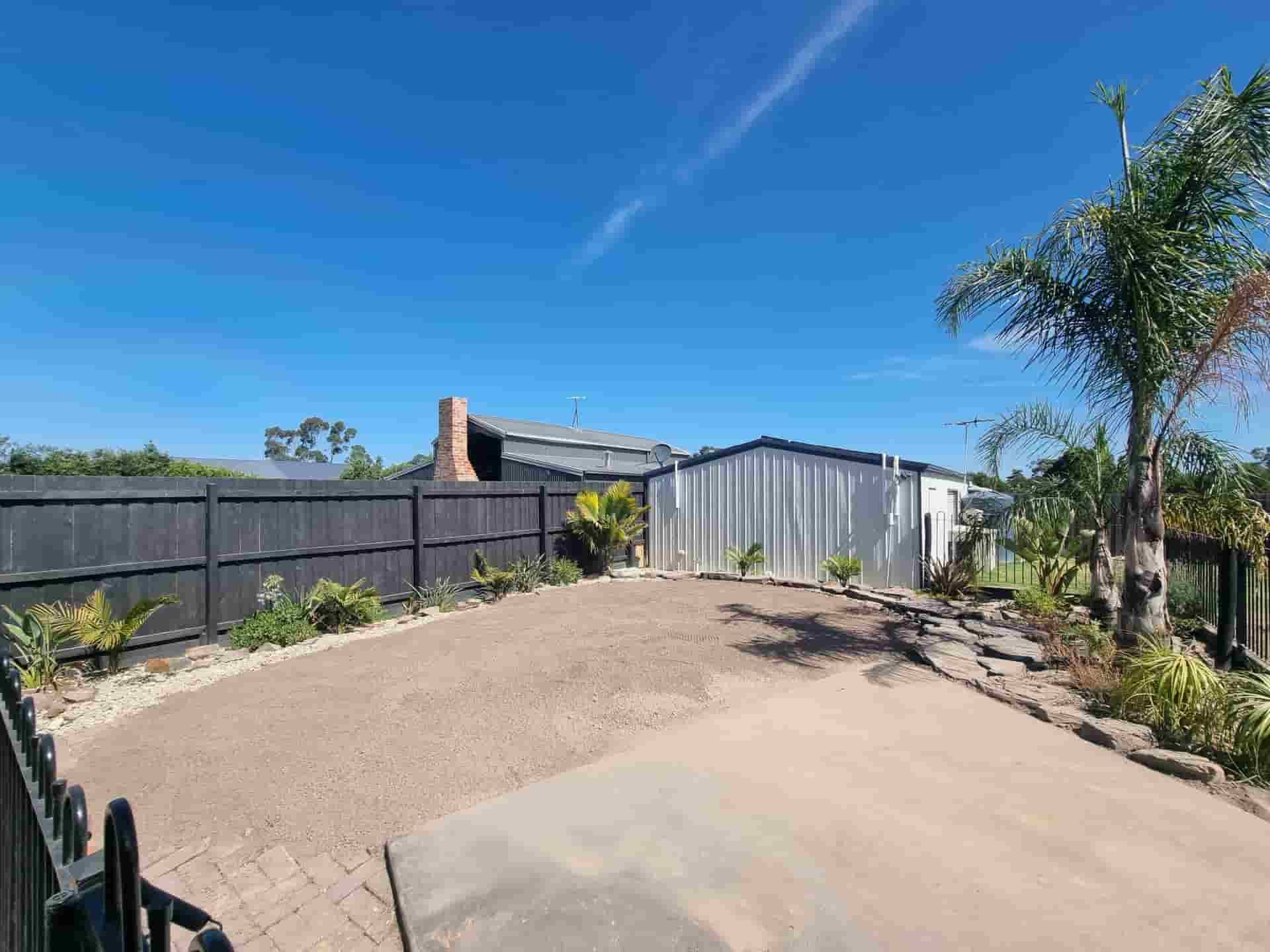 Driveway With Black Fence, Corrugated Metal Shed, Palm Tree, and Blue Sky — All Over Pool Removals in Lilydale, VIC