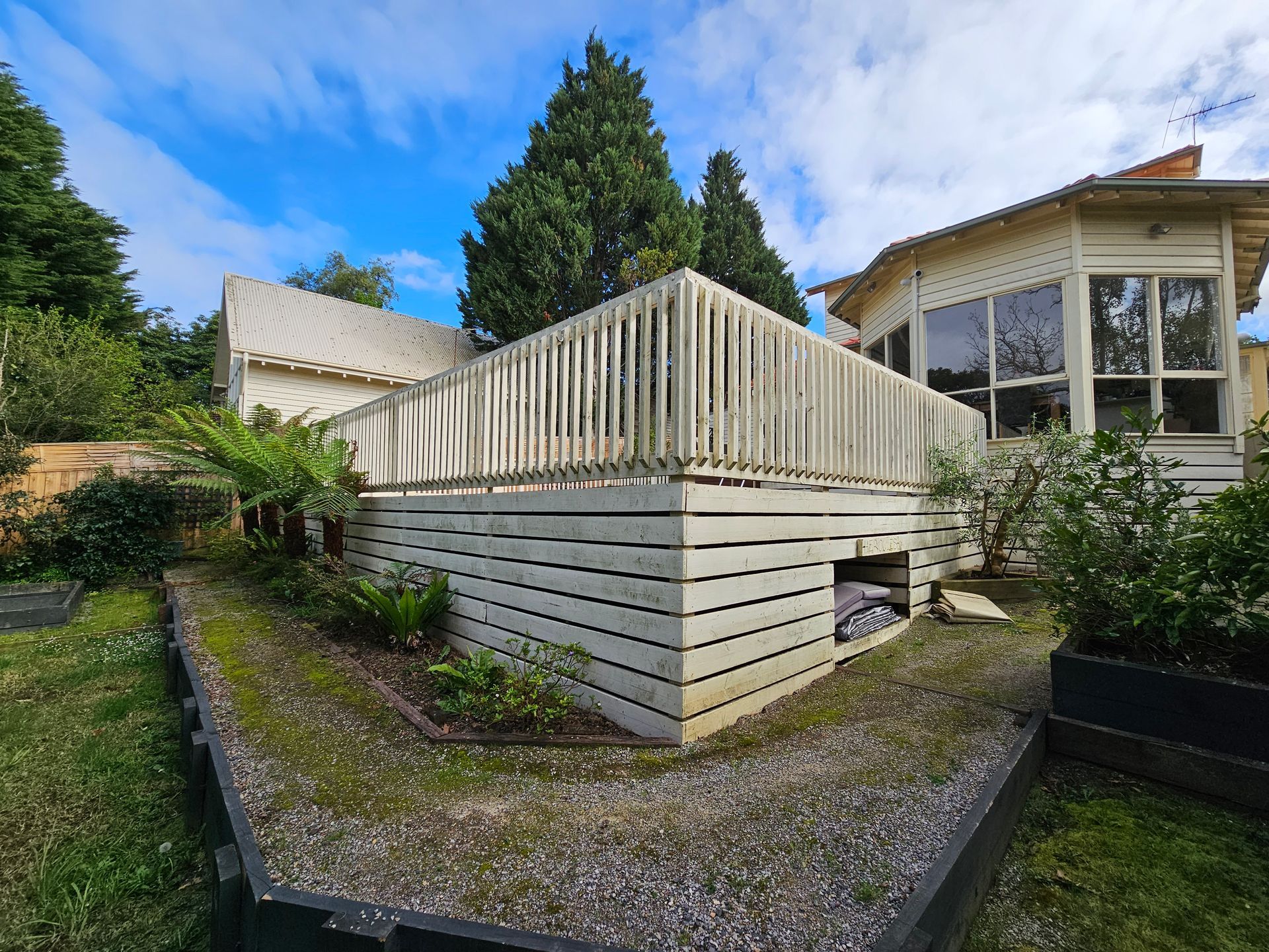 Raised Wooden Deck With White Railings in a Landscaped Backyard Under a Blue Sky — All Over Pool Removals in Beaumaris, VIC