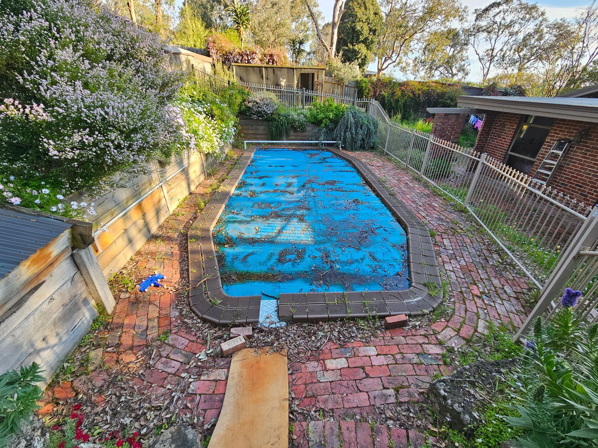 A Backyard With an Empty Blue Pool, Red Brick Patio, and Cloudy Sky — All Over Pool Removals in Upwey, VIC