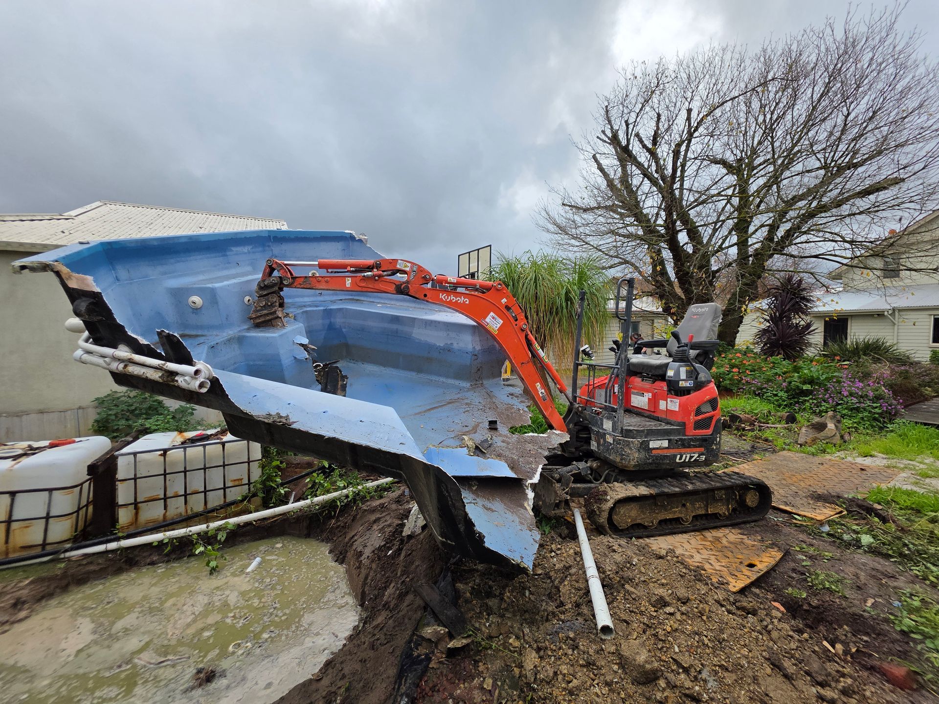 Excavator Lifting a Large Blue Boat Hull in a Muddy Yard — All Over Pool Removals in Upwey, VIC