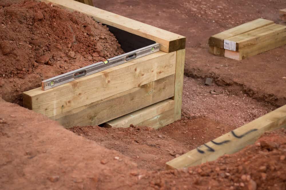 Wooden Retaining Wall Under Construction in Red Soil; a Level Rests on the Timbers — All Over Pool Removals in Beaumaris, VIC