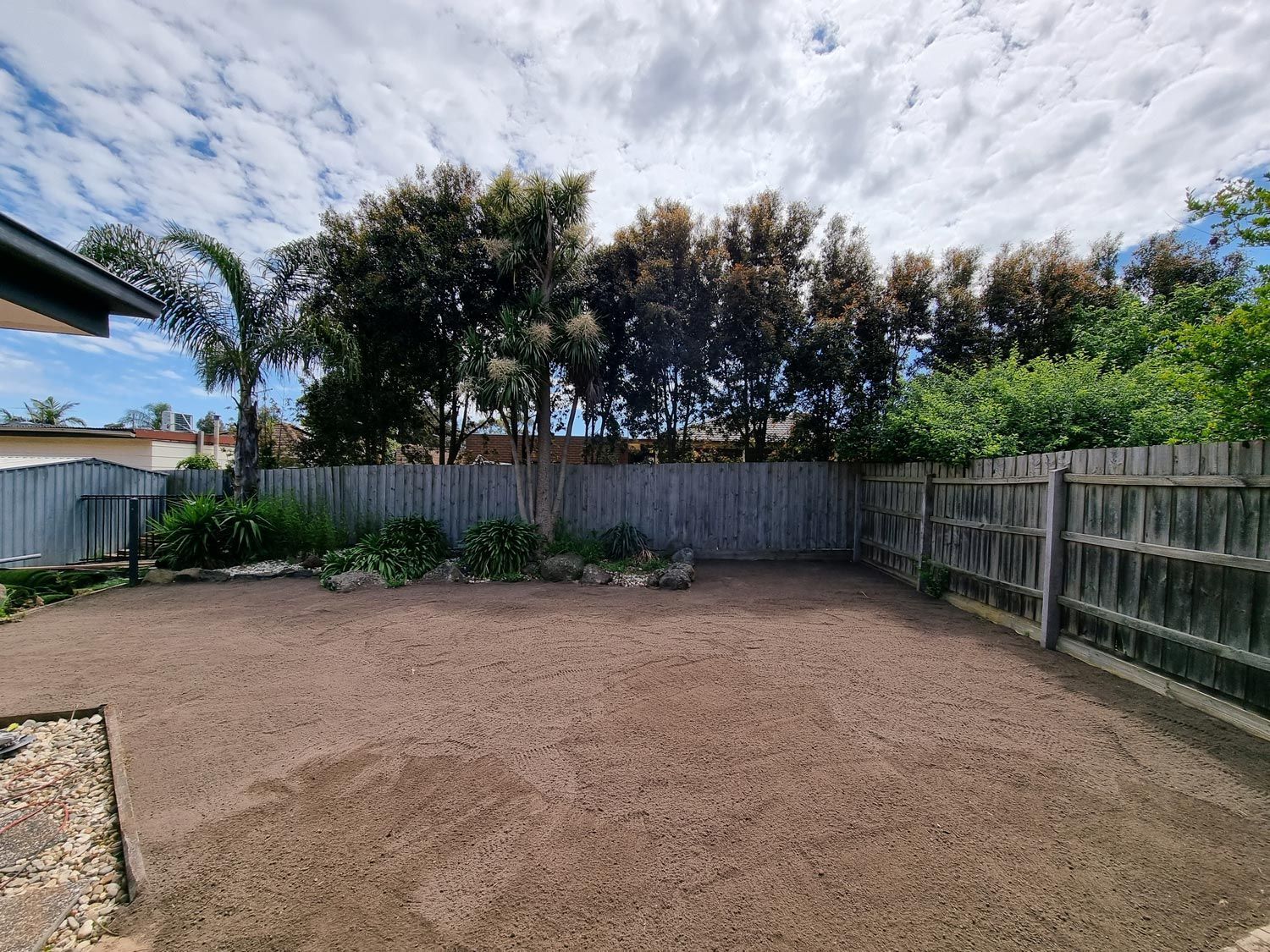 Backyard With Gravel Ground, Wooden Fence, Trees, and Cloudy Sky — All Over Pool Removals in Upwey, VIC 
