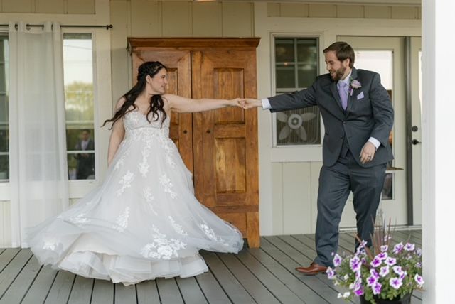 Bride and groom dancing on a porch. The bride in a white gown twirls; the groom smiles, holding her hand.